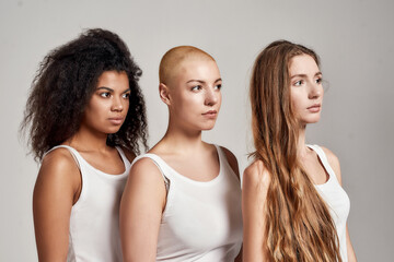 Portrait of three confident young diverse women wearing white shirts looking aside while posing...