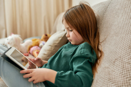 A small cute girl fully immersed into a videogame on her tablet while sitting on a sofa