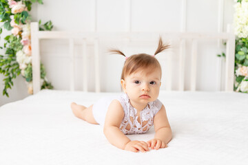 Fototapeta premium cute baby girl six months old lying in a bright beautiful room on a white bed