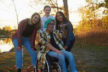 Disabled teen in a wheelchair with multi ethnic group of friends taking a group selfie.