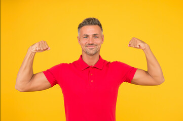 Strong athletic guy smile in red tshirt flexing muscular arms yellow background, strength