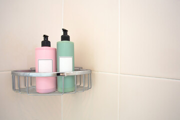 Two pastel colored soap dispensers in shower rack against tiled wall, modern design with blank label