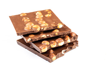 Pieces of milk chocolate with whole hazelnuts stacked in a stack on a white background