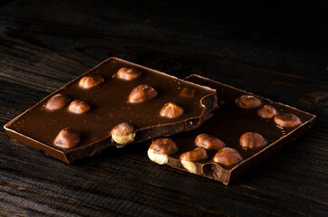 Two pieces of milk chocolate with whole hazelnuts on a dark wooden background