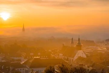 Fotobehang Cityscape of Graz with Church of the Sacred Heart of Jesus and historic buildings, in Graz, Styria region, Austria, at sunrise. Beautiful foggy morning over the city of Graz, in autumn © Aron M  - Austria