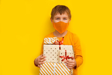 Kid boy wearing medical face mask with Christmas gift boxes on yellow background. monochrome....