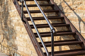 Close up view of a metal fire escape stairs attached to an antique beige color limestone block wall texture background, in bright sunlight with copy space