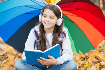 perfect autumn day of cheerful girl under colorful umbrella listen music and read book in...