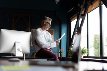 Casual Grey-haired Mature man reading paper in his office