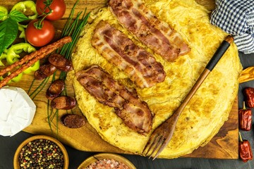 Egg omelette with bacon and sausage. Omelette with tomatoes,  green onion on wooden plate. Frittata - italian omelet. Top view. Flat lay.