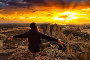 Obraz premium Man enjoying the Beautiful American Mountain Landscape. Arms Open. Taken in Smith Rock, Redmond, Oregon, America. Dramatic Sunset Artistic Render. Concept: Adventure, Holiday and Travel