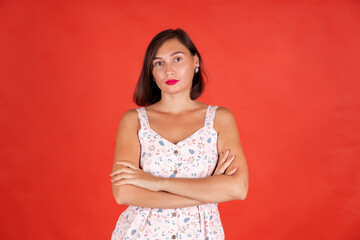  young woman staring intently at the camera with folded arms  over  red colored background