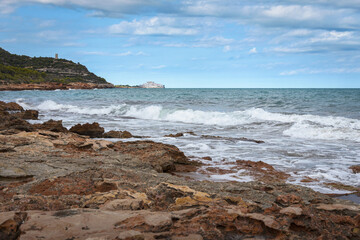 Fototapeta na wymiar Sea waves break against the rocky coastline with Peniscola in the background, Castellon, Spain
