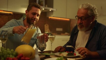 Senior father and adult son eating meal at table. Man pouring juice into glass