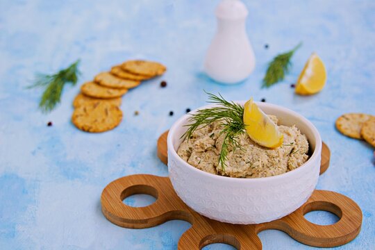 Appetizer, fish pate from mackerel, boiled eggs and onions in a white ceramic bowl on a blue concrete background.
