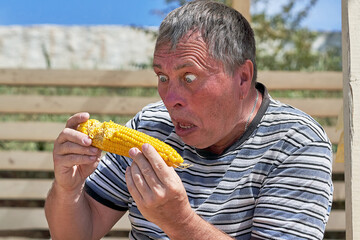 Freak with bulging eyes and open mouth holding an ear of corn