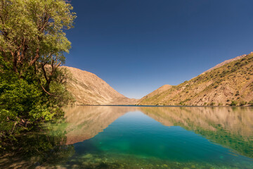 Mountain lake of Gahar, Iran in the Zagros mountains, with a few trees nearby - obrazy, fototapety, plakaty