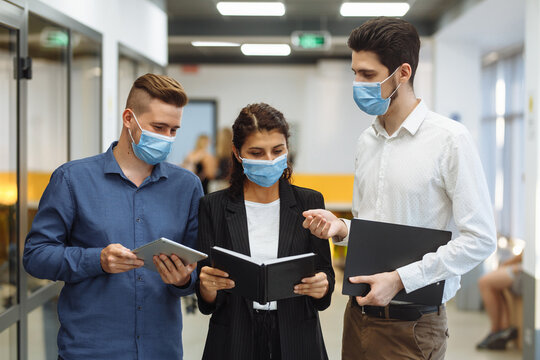 Three collegues discuss business plan during the break at the office. Coronavirus pandemic measures at work. Group of collegues stay safe wearing medical masks. Health protection concept.