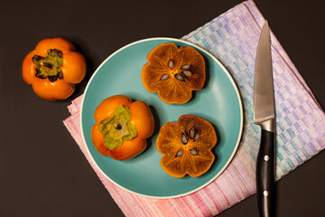 Halves and whole of ripe persimmon fruit on a plate, top view.