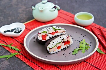 Sushi sandwiches onigirazu with baked duck, spinach and sweet pepper on a brown clay plate on a dark concrete background.
