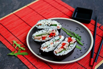 Assorted sushi sandwiches onigirazu with baked duck, spinach and sweet pepper and with salmon and cream cheese on a brown clay plate on a dark concrete background.