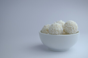 Round candies in a white plate covered with coconut shavings on a white background. 