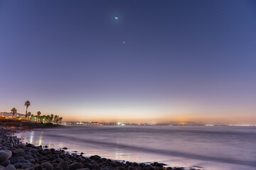Waning moon with Venus and constellation stars lighting the sky as dawn breaks over the surfing point break. © motionshooter