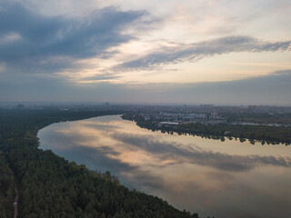 Aerial drone view. Lake on the outskirts of the city. The lake reflects the sky in the rays of the sunset. Cloudy.