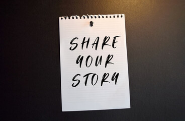 Paper note with SHARE YOUR STORY written on black slate board