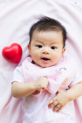 Cute asian baby smile and lay on bed with red heart and love