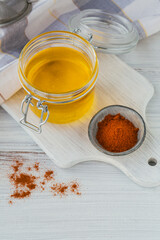 Homemade Ghee or clarified butter in a jar and paprika powder on white wooden table.