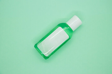 Green little bottle of hand sanitizer on mint color background