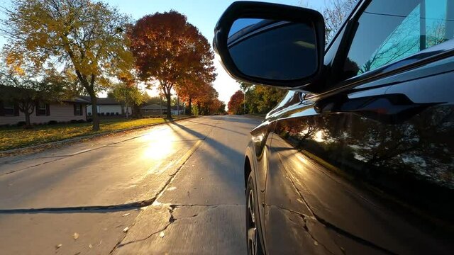 Driving a black SUV car down a suburban street in fall season. Colorful trees, red orange yellow foliage, sunset sun shining. The Autumn colors 