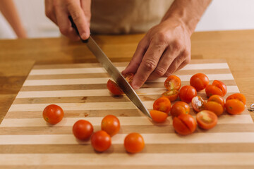 Male hands slicing cherry tomatoes on a cooking board.