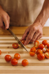 Male hands slicing cherry tomatoes on a cooking board.