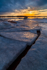 Winter landscape with frozen ice sheets floating on a lake during a beautiful sunset in...