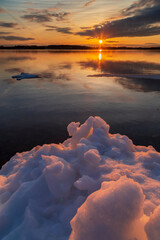 Serene winter landscape with frozen ice sheets floating on a lake during a late sunset in...