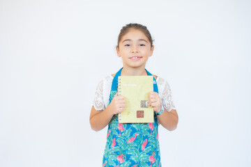 Portrait of a little girl in the kitchen dressed as a cook smiling and holding a cookbook in her hand. Concept of: nutrition, cooking school, education and family.