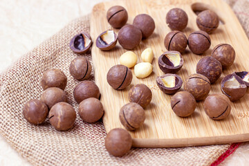 Brown macadamia nuts with wooden cutting board on light textile background.