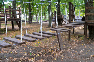 Fototapeta premium The bridge of logs tied to the ropes. lonely Broken bridge. Close up. Without children. Autumn park. Painted wooden plank. rope Park for kids in the green forest.