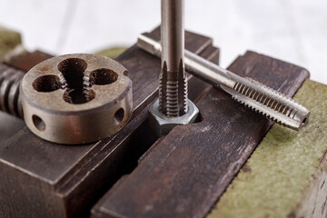 Threading a metal nut in a vice. Minor locksmith work in the workshop.