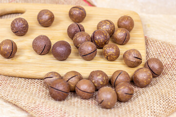 Brown macadamia nuts with wooden cutting board on light textile background.