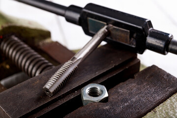 Threading a metal nut in a vice. Minor locksmith work in the workshop.