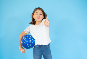 Little girl with the ball over blue with thumb up over blue background