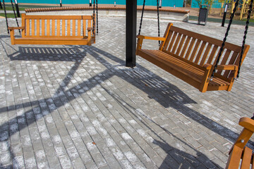 New swing bench in the park. Swing in the form of a wooden park bench. Swing in the recreation area.