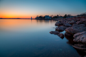 Long exposure photo of the rocky beach and cool sunset with a lighthouse in the distance....