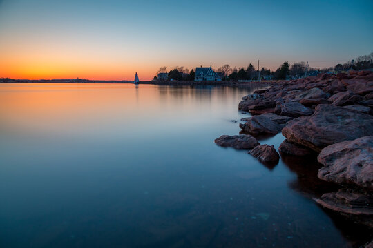 Long exposure photo of the rocky beach and cool sunset with a lighthouse in the distance. Charlottetown Prince Edward Island, Canada.