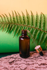 Bottle of cosmetic oil with a dropper on a green background with fern leaves and tree bark. Spa and wellness concept