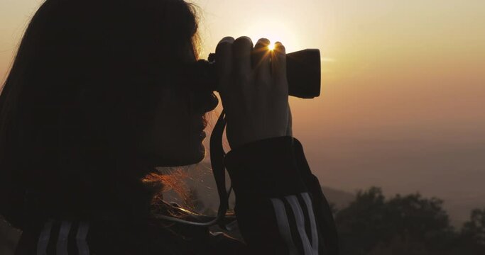 Silhouette of female watching through binocular at sunset. Female explorer concept. Hiking recreation concept. 