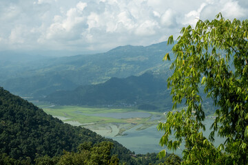An aerial view of the hills near Pokhara, Nepal, and Lake Phewa, with white cumulus clouds above them